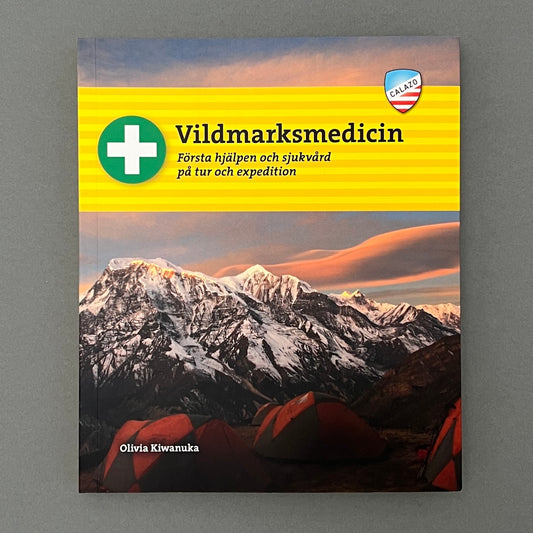 A yellow colored book called "Vildmarksmedicin" with a picture of a mountain on the cover laying on a gray background