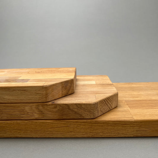 A group of three different sized wooden cutting boards laying on top of each other on a gray background