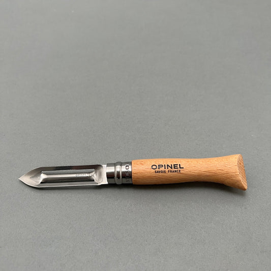 A folding stainless steel peeler from Opinel with a wooden handle laying on a gray background