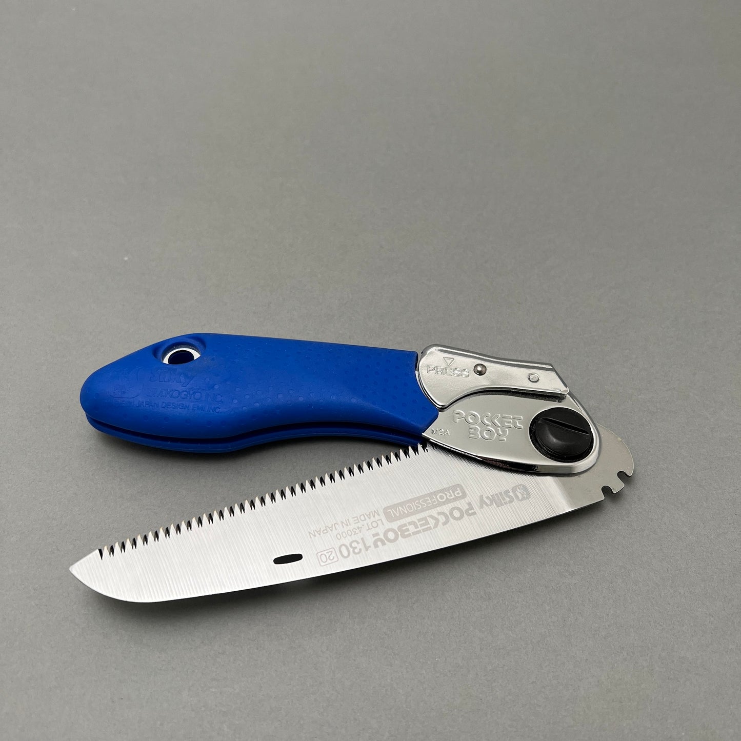 A foldable hand saw laying on a gray background  Edit alt text